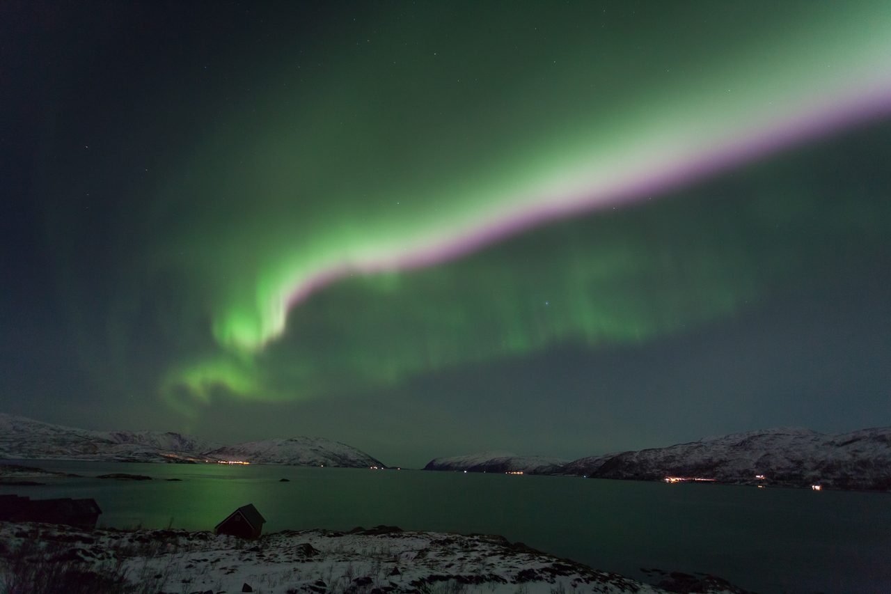 Green and purple curtains of the aurora borealis over a fjord near Tromso