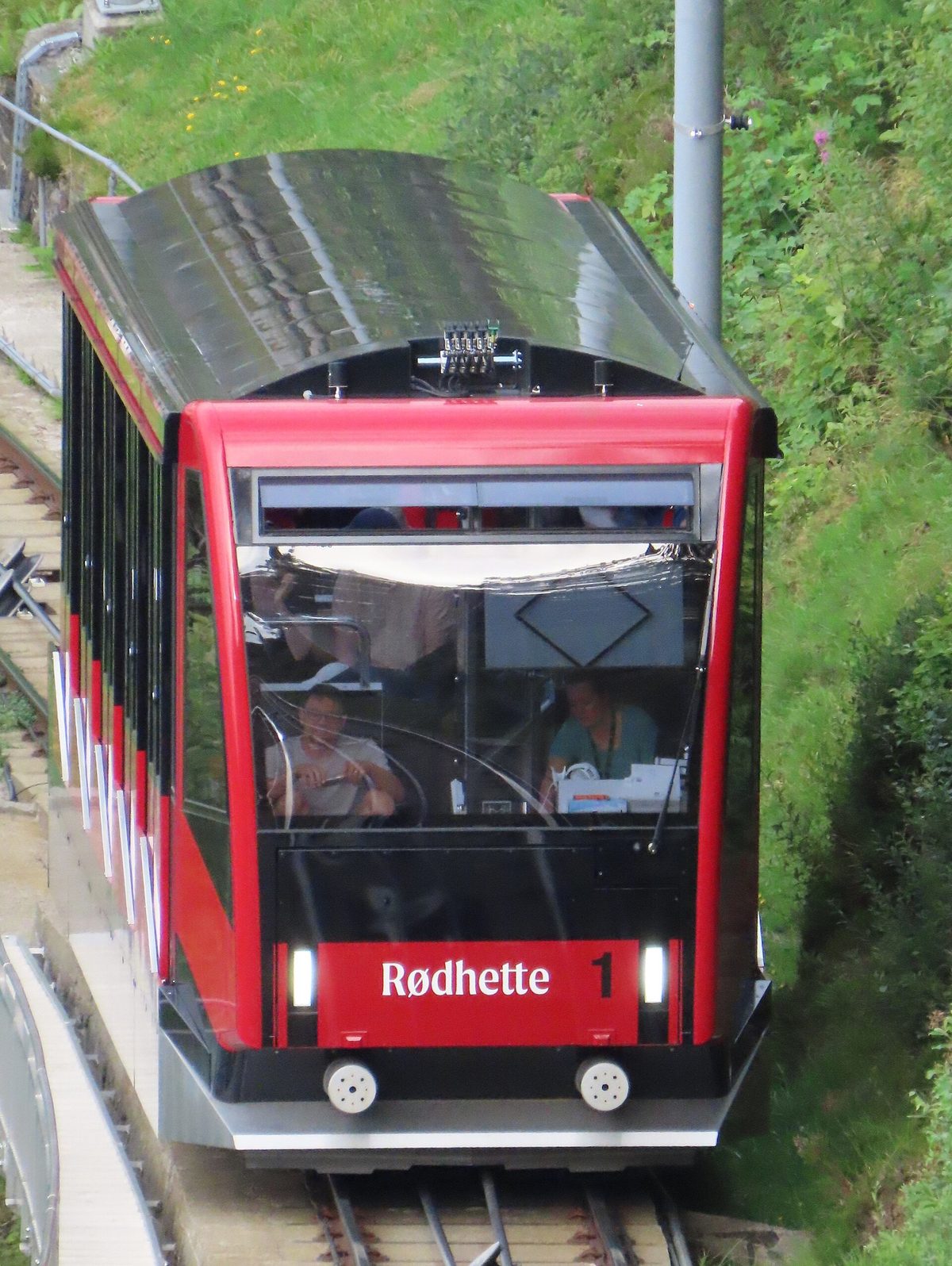 A red Floibanen funicular car climbing toward Mount Floyen above Bergen