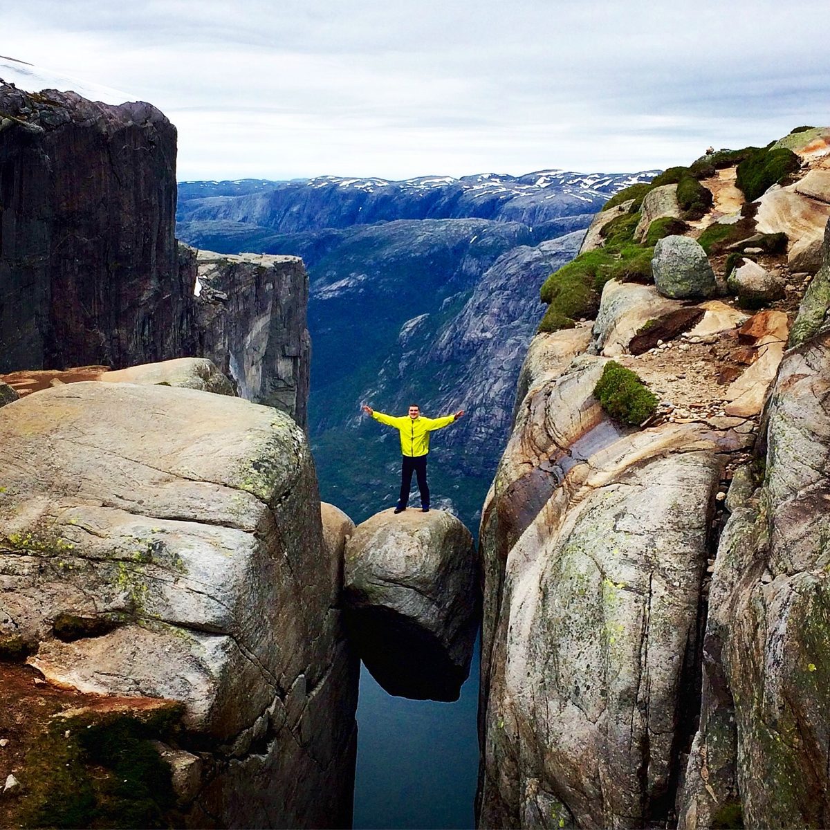 Hiker standing on the Kjeragbolten boulder wedged in a crevasse 1,000 metres above the Lysefjord