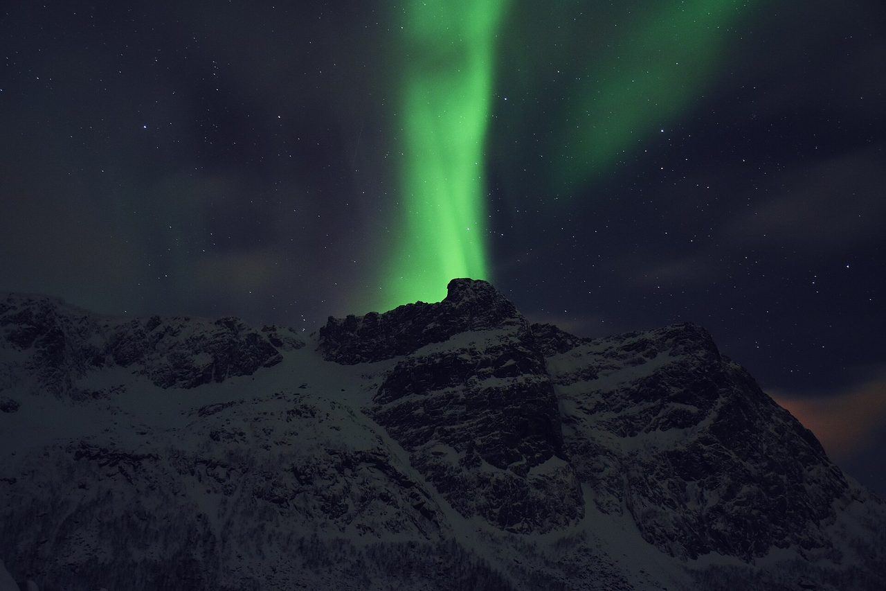 The northern lights glowing over snowy peaks in northern Norway