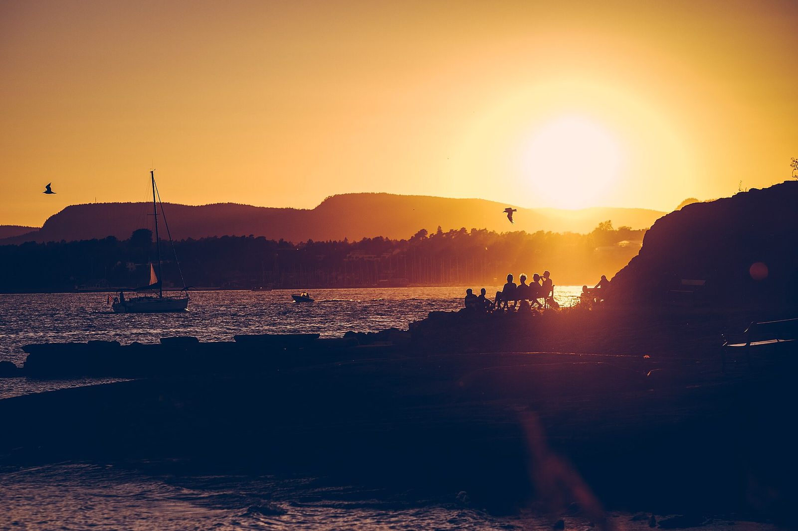 Sunset over the Oslofjord with a sailboat and people relaxing on the rocks in summer